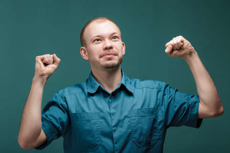 portrait of young successful smiling doctors raises his hands up on  blue background. gesture of victoryの写真素材