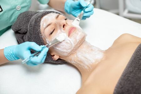 beautician applies face mask on beautiful young woman in Spa salon. cosmetic procedure skin care. Microdermabrasionの写真素材