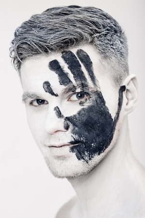 Young man with black hand print on white face. Closeup Portrait.  Professional Fashion Makeup. fantasy art  makeupの写真素材