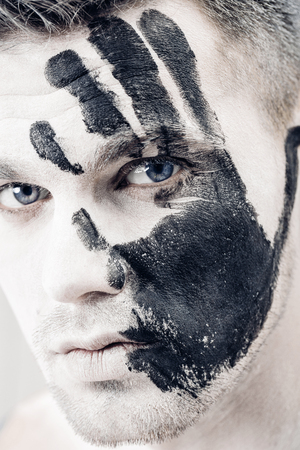 Young man with black hand print on white face. Closeup Portrait.  Professional Fashion Makeup. fantasy art  makeupの写真素材