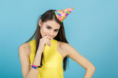 young attractive smiling woman with birthday hat and whistle on blue background. celebration and partyの写真素材