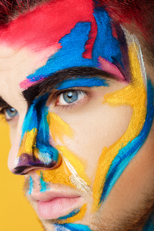 portrait of young man with colored face paint on yellow background. Professional Makeup Fashion. fantasy art makeupの写真素材