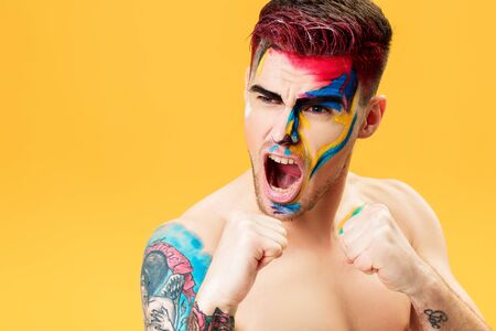 portrait of young man with colored face paint on yellow background. Professional Makeup Fashion. fantasy art makeupの写真素材