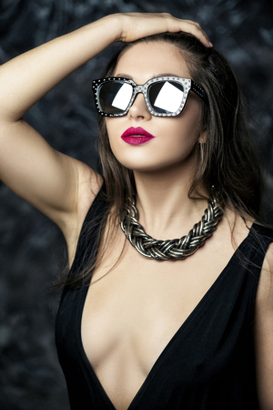 portrait of a young sexy and seductive brunette woman with red lipstick in black dress and sunglassesの写真素材