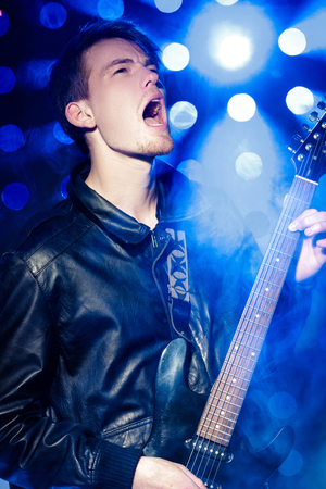 young rock musician playing electric guitar and singing. Rock star on background of spotlightsの写真素材