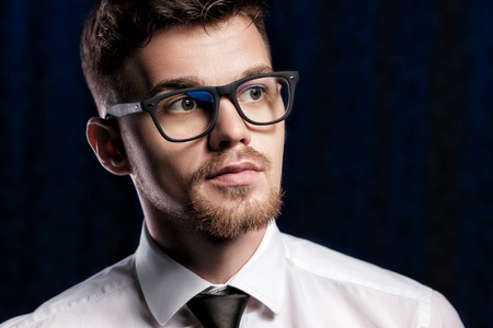 Portrait of handsome young man with glasses and white shirt on dark backgroundの写真素材