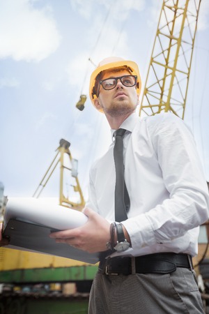 Engineer builder in a helmet holds drawings at construction siteの写真素材