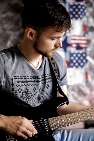 Young handsome musician playing electric guitar on dark backgroundの写真素材