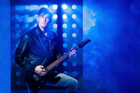 young attractive rock musician playing electric guitar and singing. Rock star on background of spotlightsの写真素材