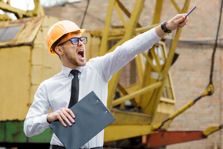 Engineer builder in a helmet holds drawings and shows by hand at construction siteの写真素材