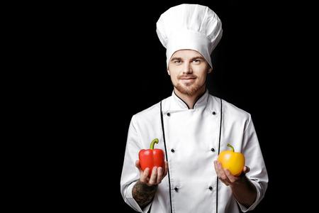 Young bearded man chef In white uniform holds bell peppers on  black backgroundの写真素材
