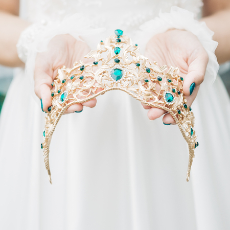 brides hands hold beautiful crown with green gemsの写真素材