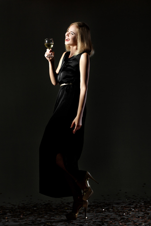 Beautiful blonde woman with glass of white wine on black backgroundの写真素材