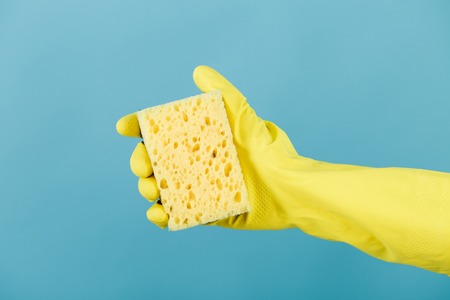hand  in yellow glove holding sponge on blue background. cleaningの写真素材