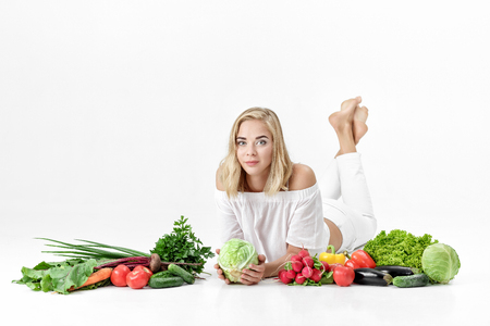 Beautiful blond woman in white clothes and lots of fresh vegetables on white backgroundの写真素材