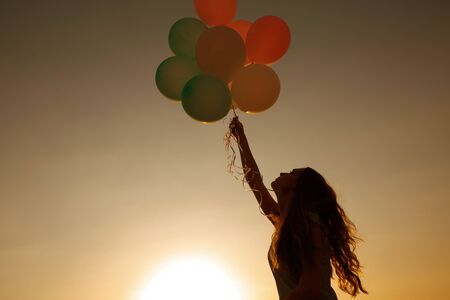 silhouette of young woman with flying balloons against the sky.の写真素材