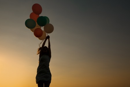 silhouette of young woman with flying balloons against the sky.の写真素材