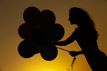 silhouette of young woman with flying balloons against the sky.の写真素材