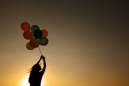 silhouette of young woman with flying balloons against the sky.の写真素材