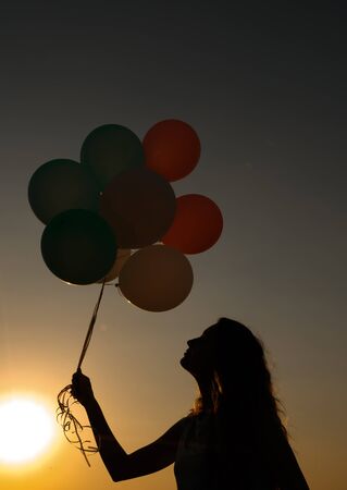 silhouette of young woman with flying balloons against the sky.の写真素材