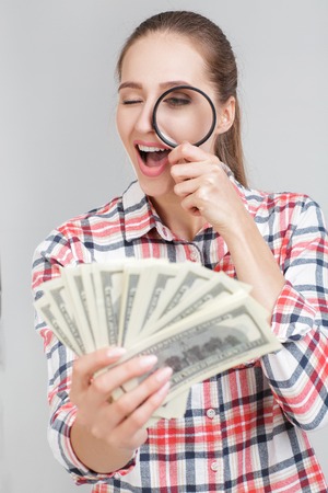 woman looks in magnifier on dollar billsの写真素材