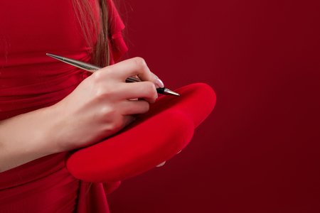 womans hand writes with a pen on her heart.の写真素材