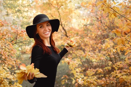 woman in dress and hat on background of autumn foliageの写真素材