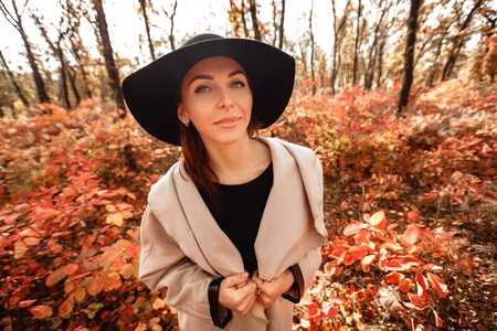 woman in dress and hat on background of autumn foliageの写真素材