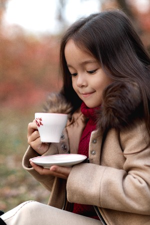 little girl drinking warm tea in autumn parkの写真素材