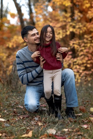 father walks with little daughter girl on background of yellow leavesの写真素材