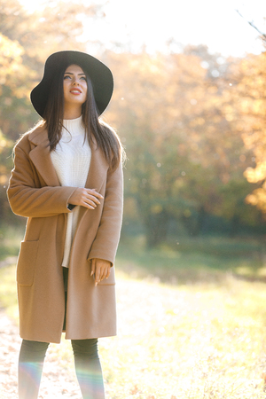 beautiful young woman in coat and black hat in parkの写真素材