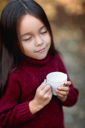 little girl drinking warm tea in autumn parkの写真素材