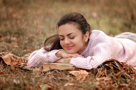 woman sitting in autumn park and reading bookの写真素材