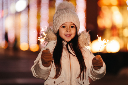 Cute smiling little girl with bengal lights on the street in the eveningの写真素材