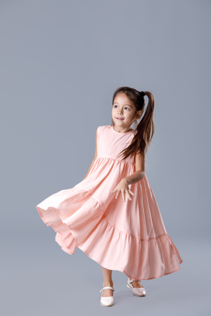 little girl in pink dress posing on gray background.の写真素材