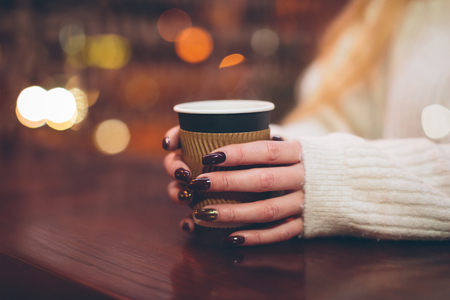 female hands holding a paper cup with hot coffee in a cafe on a cold winter eveningの写真素材