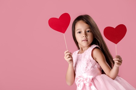cute little girl in a pink dress holding a paper heartの写真素材