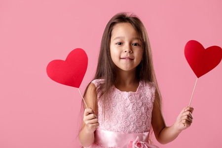 cute little girl in a pink dress holding a paper heartの写真素材