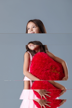 portrait of smiling cute little girl in pink dress holding big red heart on gray background. St. Valentines Dayの写真素材