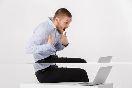 indignant young man in shirt using laptop against white backgroundの写真素材