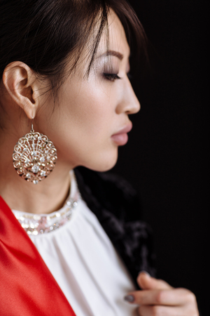 portrait of fashionable asian woman with gold earrings black background. studio shotの写真素材