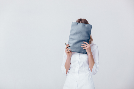 upset medical physician doctor woman in white coat covers her face with a folder.の写真素材