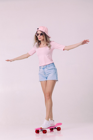beautiful woman in sunglasses, pink t-shirt and cap stands on pink skateboardの写真素材
