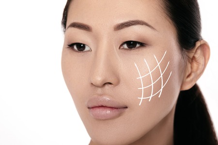 Spa portrait of attractive asian woman with arrows on her face on white background. Face lifting concept. Plastic surgery treatment, medicineの写真素材