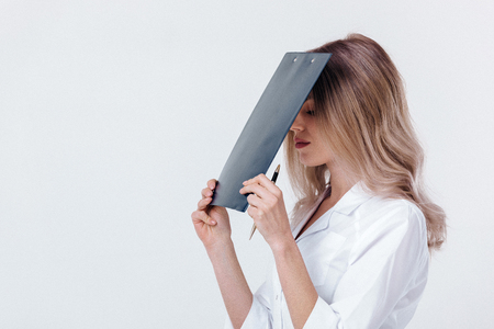 tired medical physician doctor woman in white coat holds folder with documents on light background.の写真素材