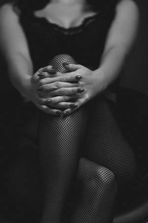 slim sexy woman in black stockings sits on a chair on a black background. black and whiteの写真素材