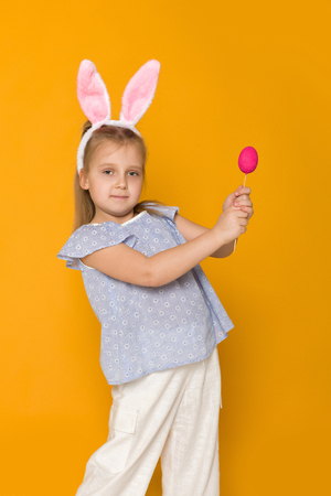 Portrait of cute little child girl with Easter bunny ears holding colorful eggs on yellow background. Happy easterの写真素材