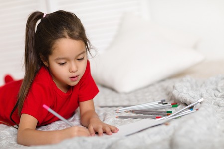 cute little child girl in red pajamas draws with pencils at home