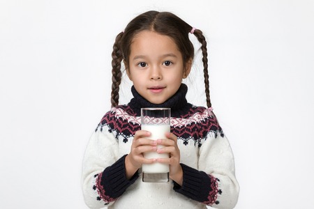 Portrait of cute little child girl holding glass of fresh milk isolated on whiteの写真素材