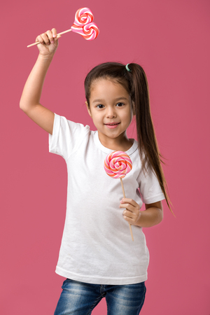 Beautiful cute little child girl with sweet candy lollipop isolated on pink backgroundの写真素材